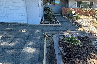 Concrete walkway and driveway installation in Riverside in progress, featuring wooden framing, rebar grid, and landscape-ready front yard hardscaping.