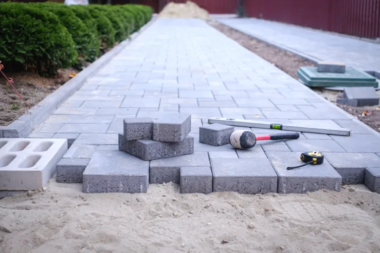 Gray concrete pavers being installed with tools and sand base on a driveway project in San Bernardino, California