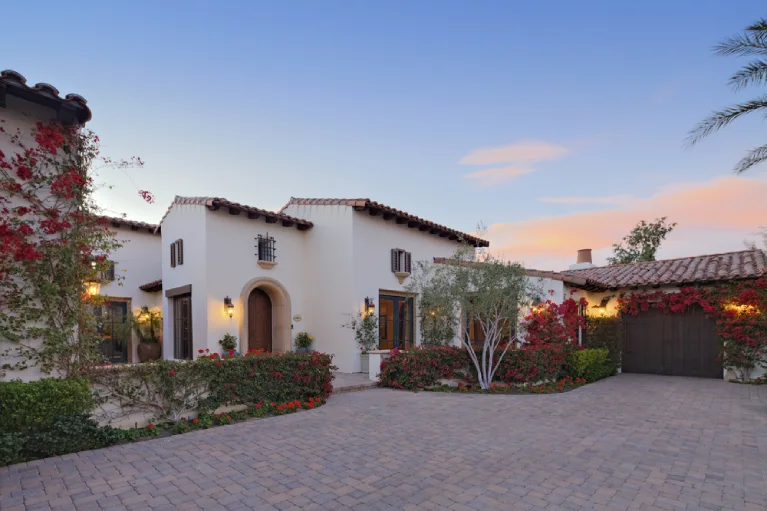 Spanish-style Southern California home with a wide Belgard paver driveway and vibrant landscaping at sunset