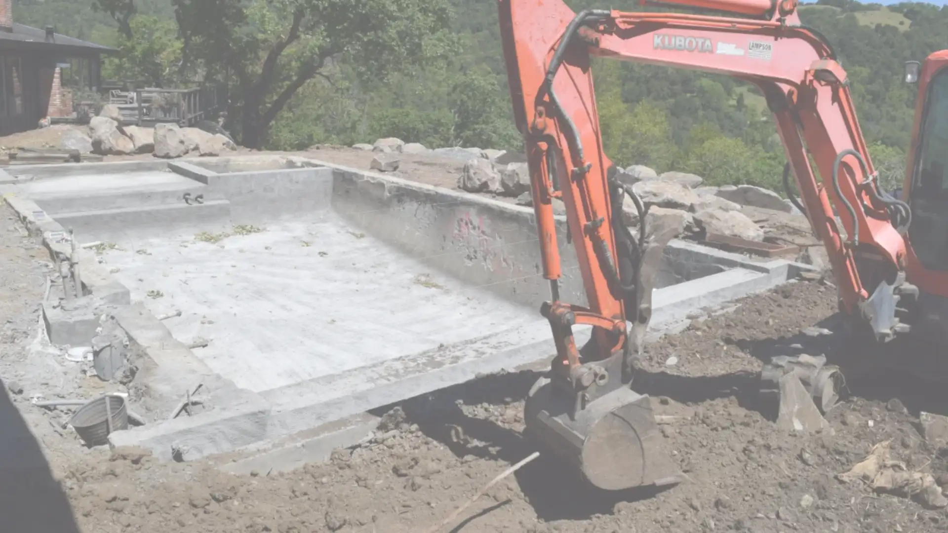 Excavator preparing a residential property for hardscaping in Southern California, with concrete pool shell and surrounding hillside landscape in view.