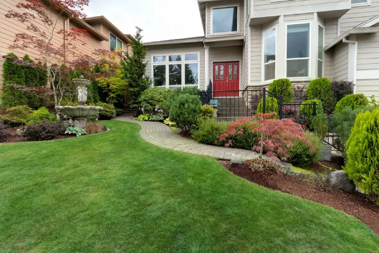 Well-maintained front yard in Orange County featuring a curved paver walkway, tiered stone fountain, and lush greenery designed by professional hardscape contractors.