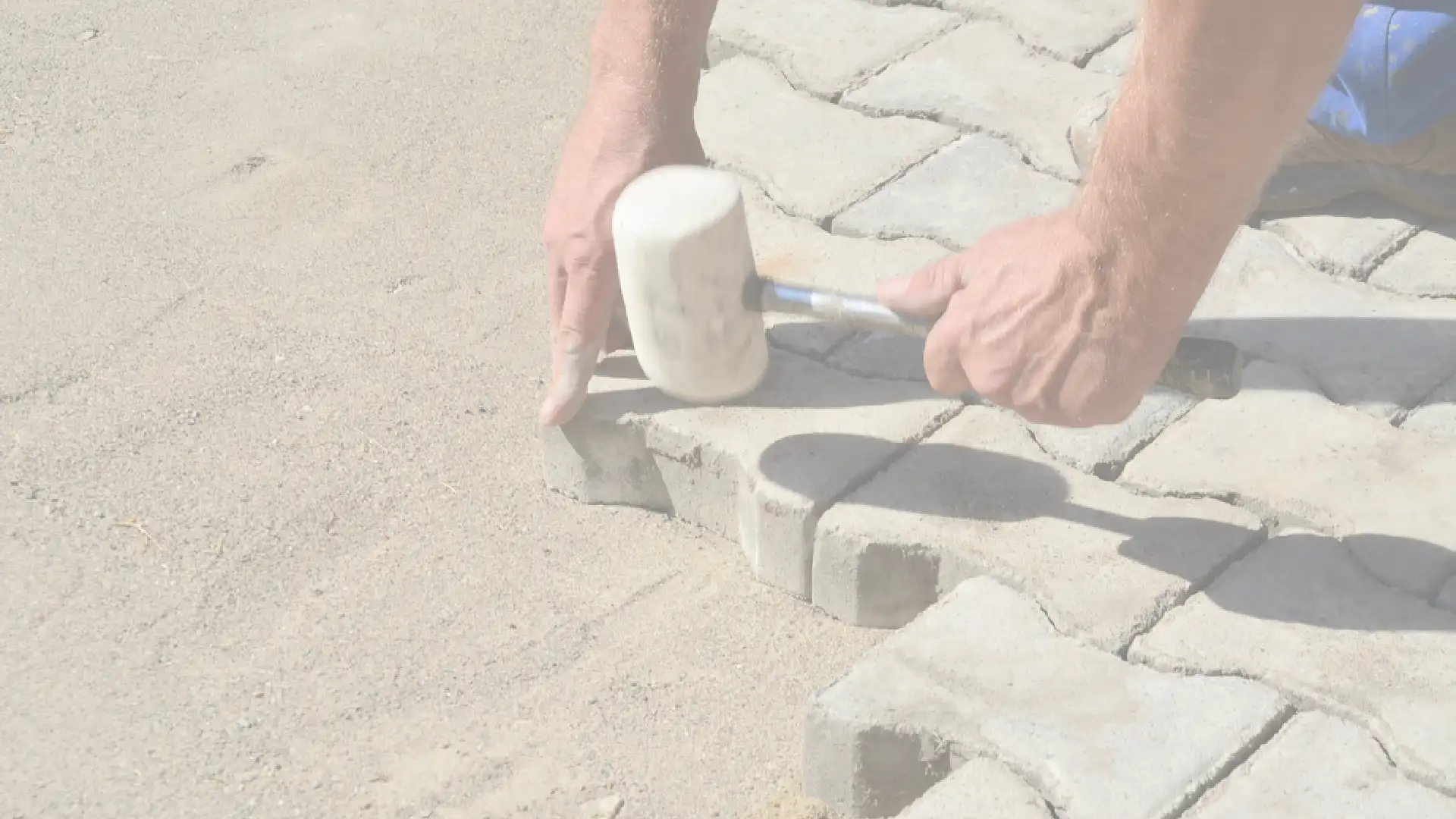 Close-up of contractor laying pavers with a rubber mallet on sand base for a Southern California home project
