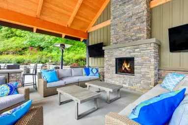 Covered outdoor living space in Mission Viejo featuring a custom stone fireplace, wood-paneled ceiling, patio seating, and built-in entertainment area.