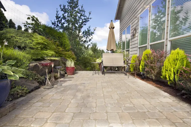 Backyard paver patio with lush greenery and a garden bench in a Southern California home