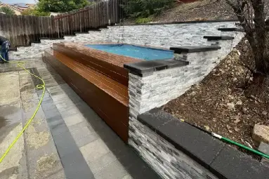 Modern raised spa in Costa Mesa surrounded by stacked stone retaining walls, paver walkway, and composite wood siding for a high-end backyard transformation.