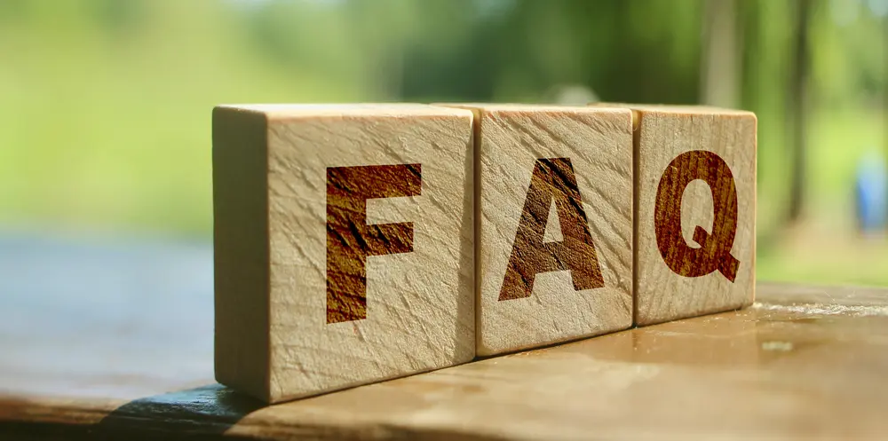 Wooden blocks spelling FAQ placed on a sunlit surface with a blurred outdoor background, symbolizing frequently asked questions