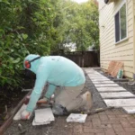 Worker installing concrete pavers over a compacted base during hardscape renovation at a Southern California home.