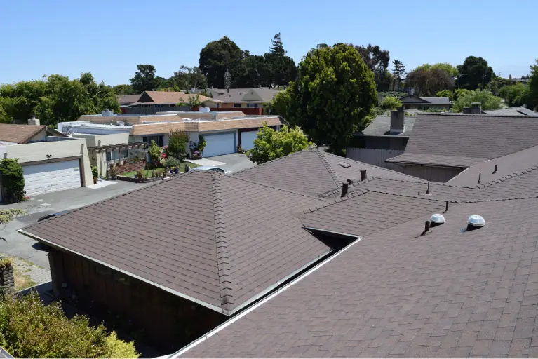 Aerial view of a neighborhood in Orange County showcasing multiple homes with brown asphalt shingle roofs, driveways, trees, and well-maintained yards on a clear sunny day.