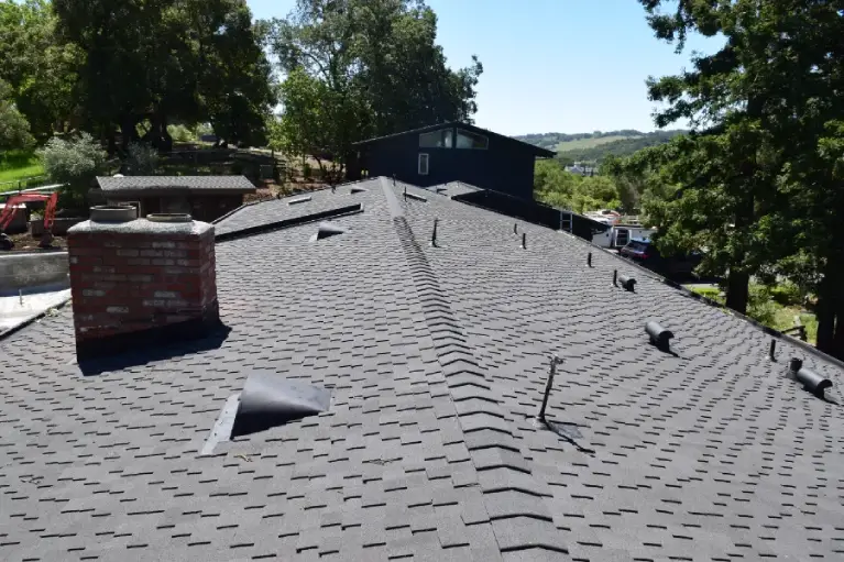 Close-up view of a newly installed asphalt shingle roof with chimney and vents, representing roofing installation, repairs, and storm protection in Southern California.