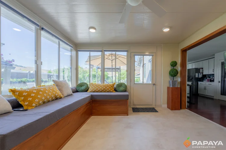 Bright sunroom interior focusing on the wall of sliding glass windows and the view of the outdoor umbrella and garden.