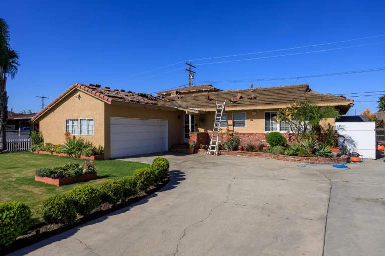 roof tear-off in progress with visible stucco damage on residential home exterior in Garden Grove CA before remodel