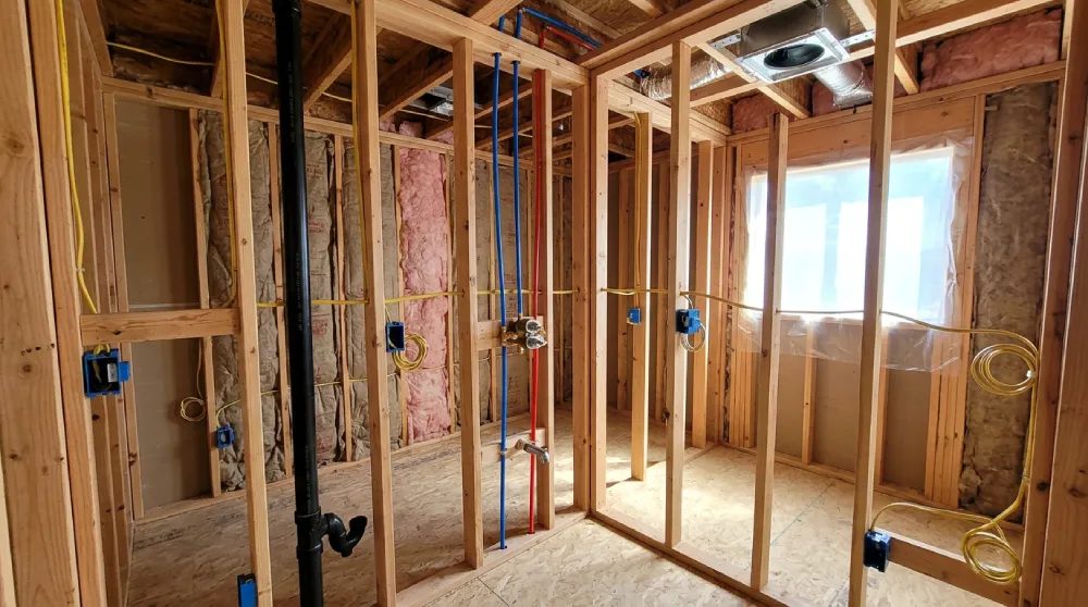 New bathroom construction in progress by Papaya Construction Group in Orange County, CA — framing, plumbing rough-in with copper supply lines and drain stack, electrical rough-in including dedicated 20-amp circuits and vacancy-sensor wiring, ceiling exhaust fan housing, and insulation showing the full general contractor scope behind a new bathroom build or whole-home addition.